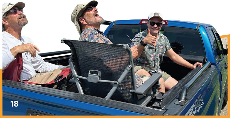 Three men sitting in a blue truck bed; one gives a thumbs-up.