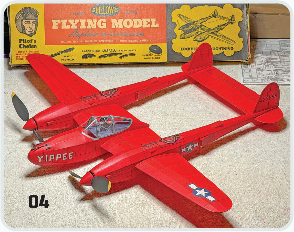 Red model airplane on carpet, "YIPPEE" on nose, vintage box and plans in background.