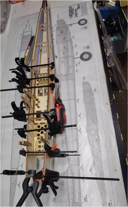 Wooden model airplane frame on blueprint with clamps.