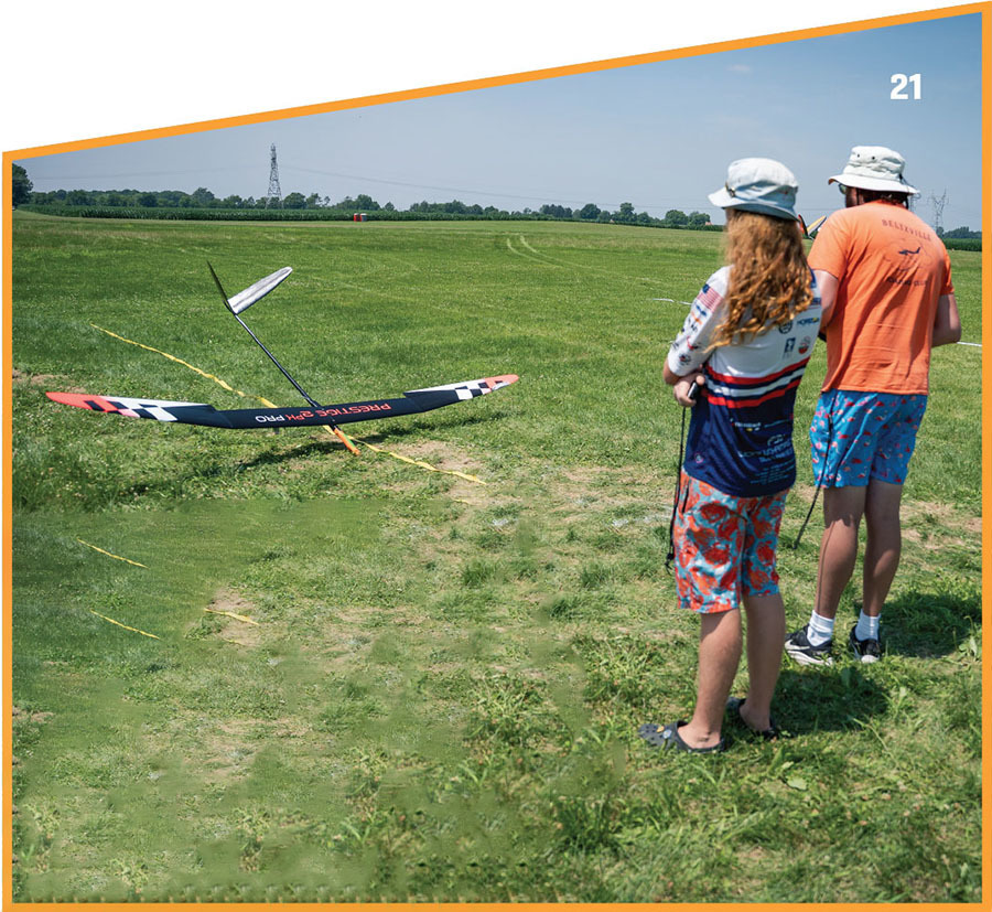 Two people flying a model glider in a grassy field, numbered 21.