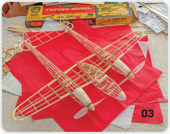Wooden biplane models on red paper, with scale airplane kit boxes in the background.