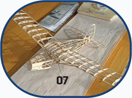 Wooden model airplane frame labeled "07" on a table.