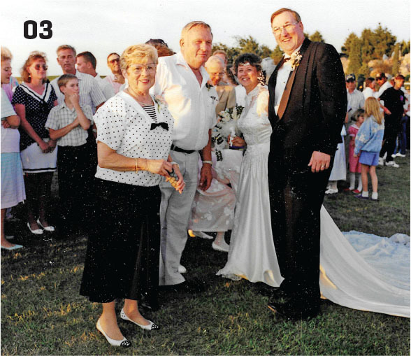 Two couples smiling at an outdoor event, including a bride and groom.
