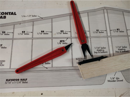 Red hobby knives on a balsa wood airplane plan.