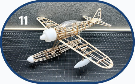 Model airplane with wooden frame on a grid cutting mat; number 11 in the corner.