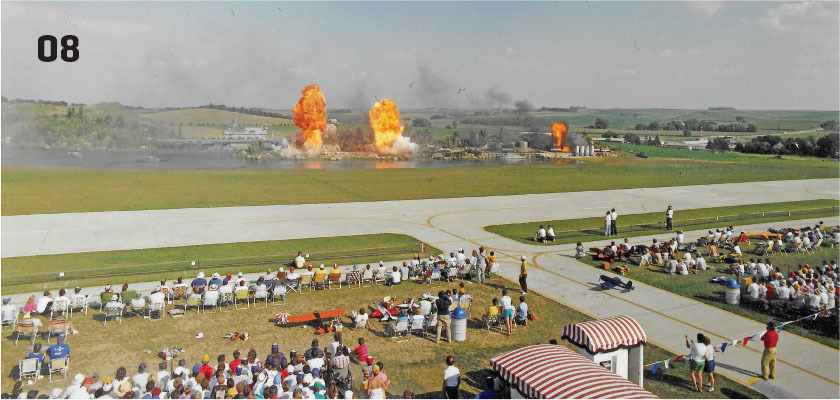 Crowd watches explosions and smoke on distant field, numbered "08" at top left.