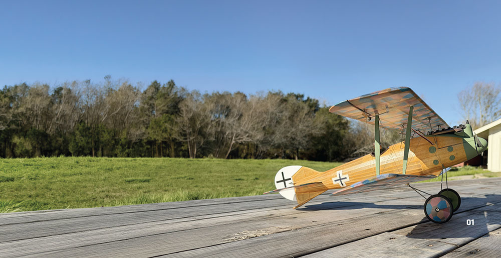 Wooden model plane on picnic table with green field and trees.
