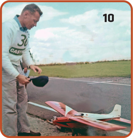 Man preparing red model airplane on airstrip, number 10 in black corner.