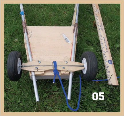 Cart with wheels on grass, measuring tape beside it, labeled "05".