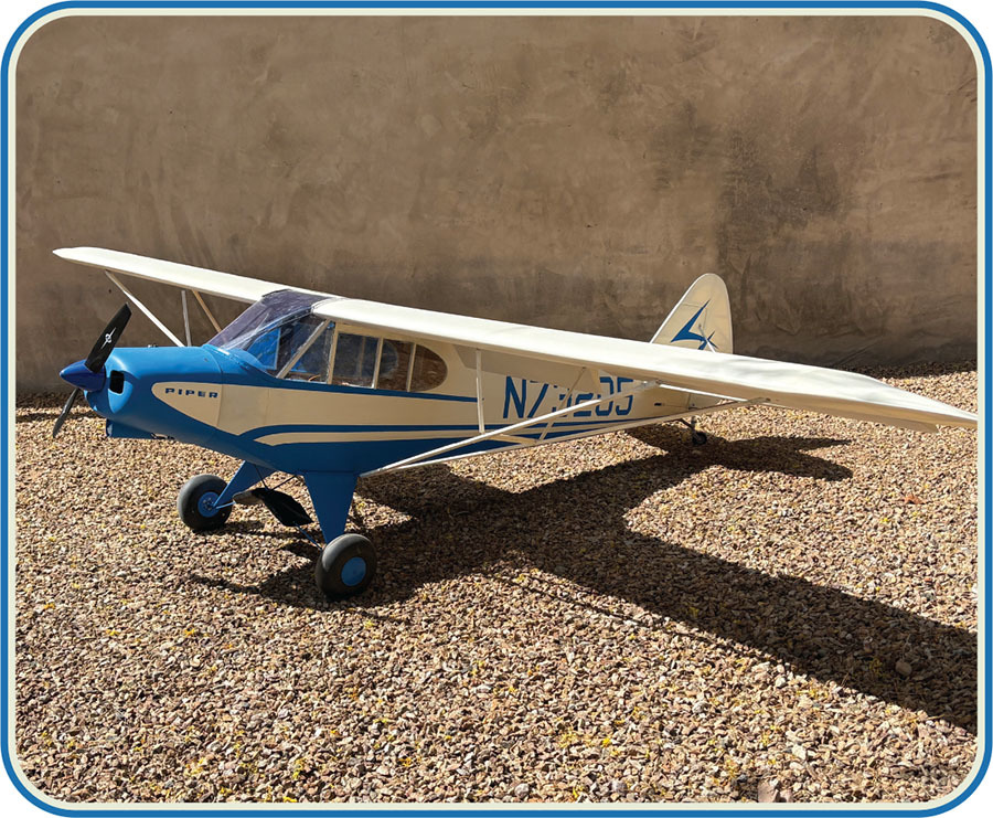 Plastic model plane on gravel, labeled "Piper" with blue and cream colors.