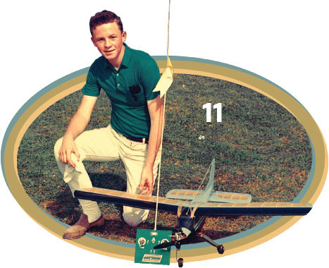 Young man kneeling on grass with model airplane and remote control, number 11 visible.