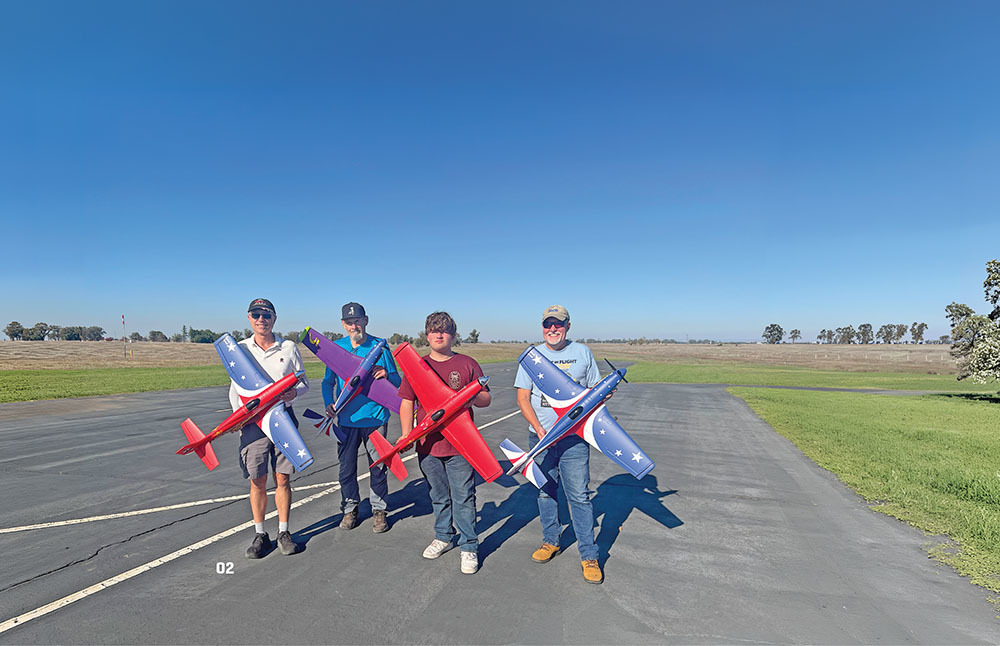 Four people holding model airplanes on an open tarmac under a clear blue sky.