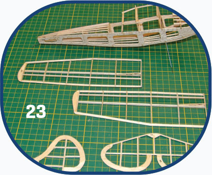 Wooden model airplane parts on a green grid mat, number 23 displayed.