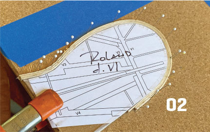 Paper pattern pinned to corkboard with "02" printed on it.