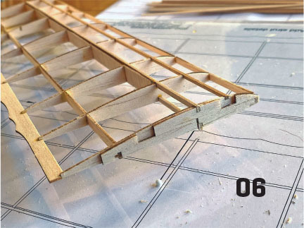 Wooden model airplane wing frame on blueprint, number 06 visible.