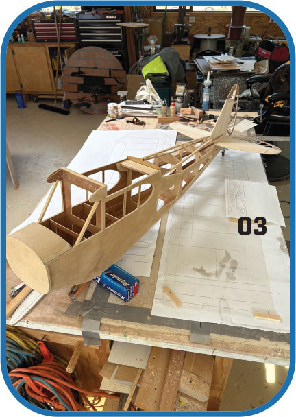 Wooden model airplane frame on a workbench, surrounded by tools and plans.