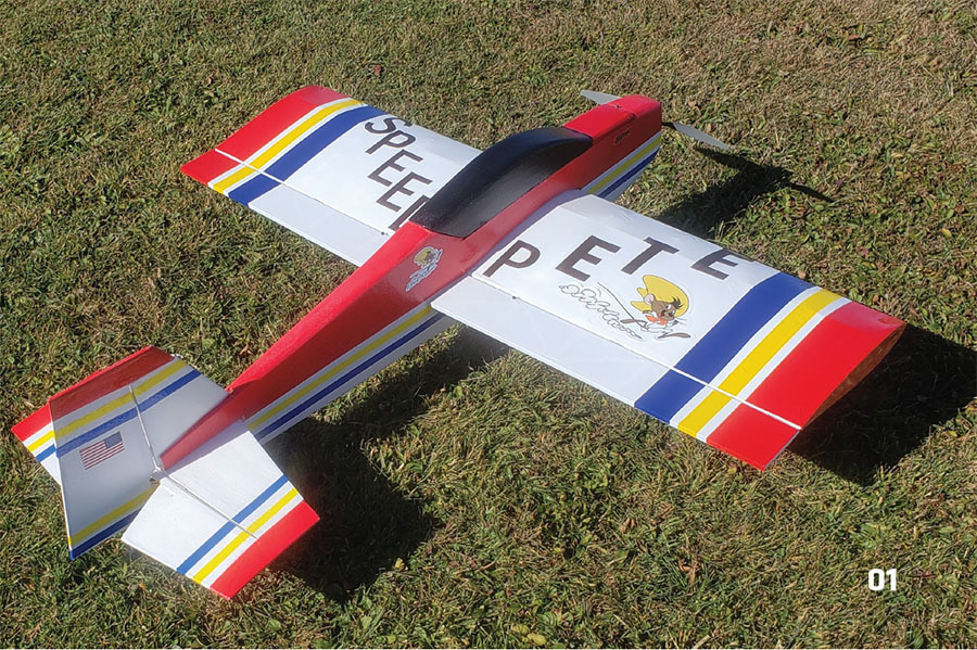 Red and white model airplane on grass, labeled "SPEED PETE" with colorful stripes.
