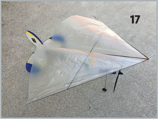 Silver kite with blue and yellow accents on concrete, number 17 displayed nearby.