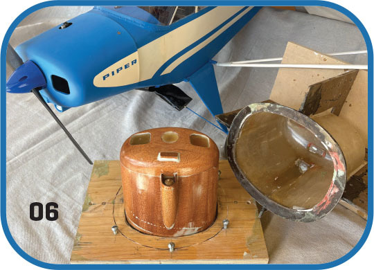 Blue model airplane with "Piper" text and wooden propeller mount.