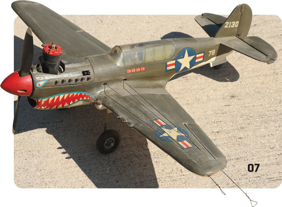 Model airplane with shark mouth art, star insignia, sand background, marked 213 and 7B.