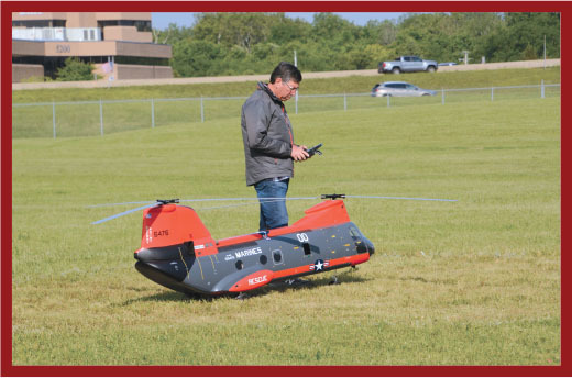 Person operating a large model helicopter in a grassy field.