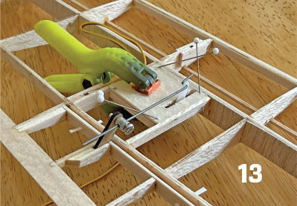 Model airplane structure with a clamp and pins on a wooden table, number 13 visible.