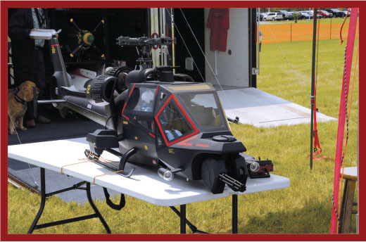 Model helicopter on a table, outdoor setting with grass and gear in background.
