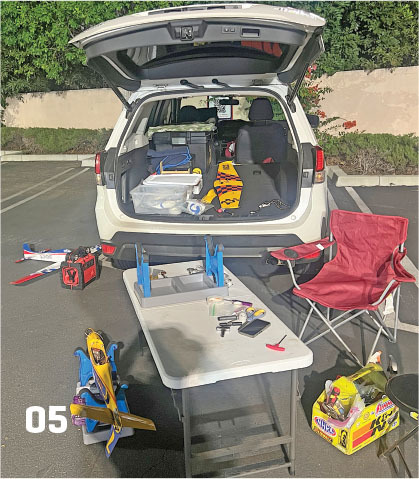 Car trunk open with model planes and table setup in a parking lot.