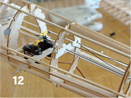 Wooden model airplane fuselage with wiring and components, number 12 displayed.