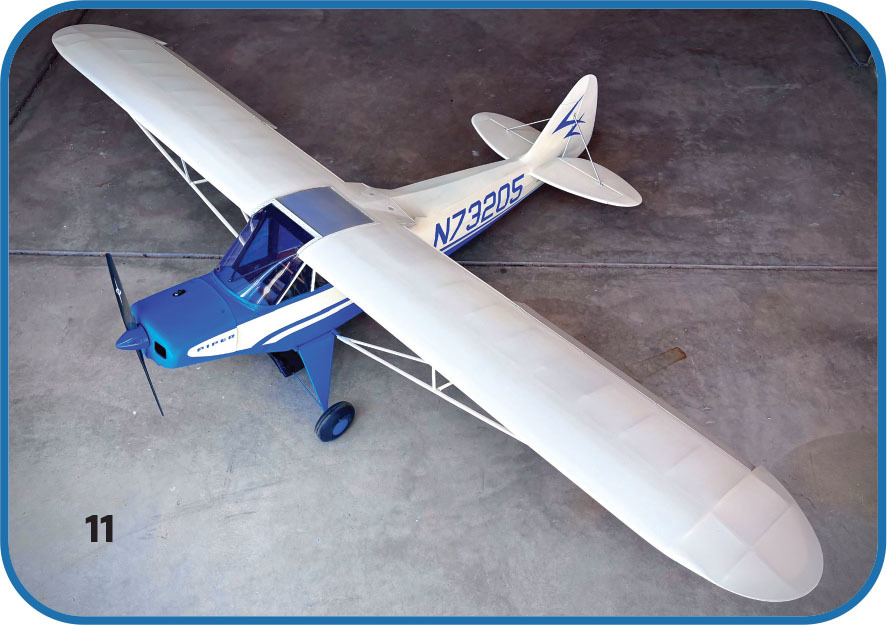 Model airplane with white wings, blue fuselage, labeled "N73205", on gray floor.