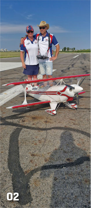 Two people in matching outfits with a model biplane on a runway.