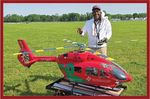 Man posing with a large red and green model helicopter on grass.