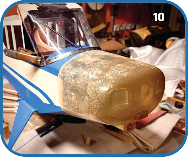 Yellow nose cover on a blue model airplane in a cluttered workshop.