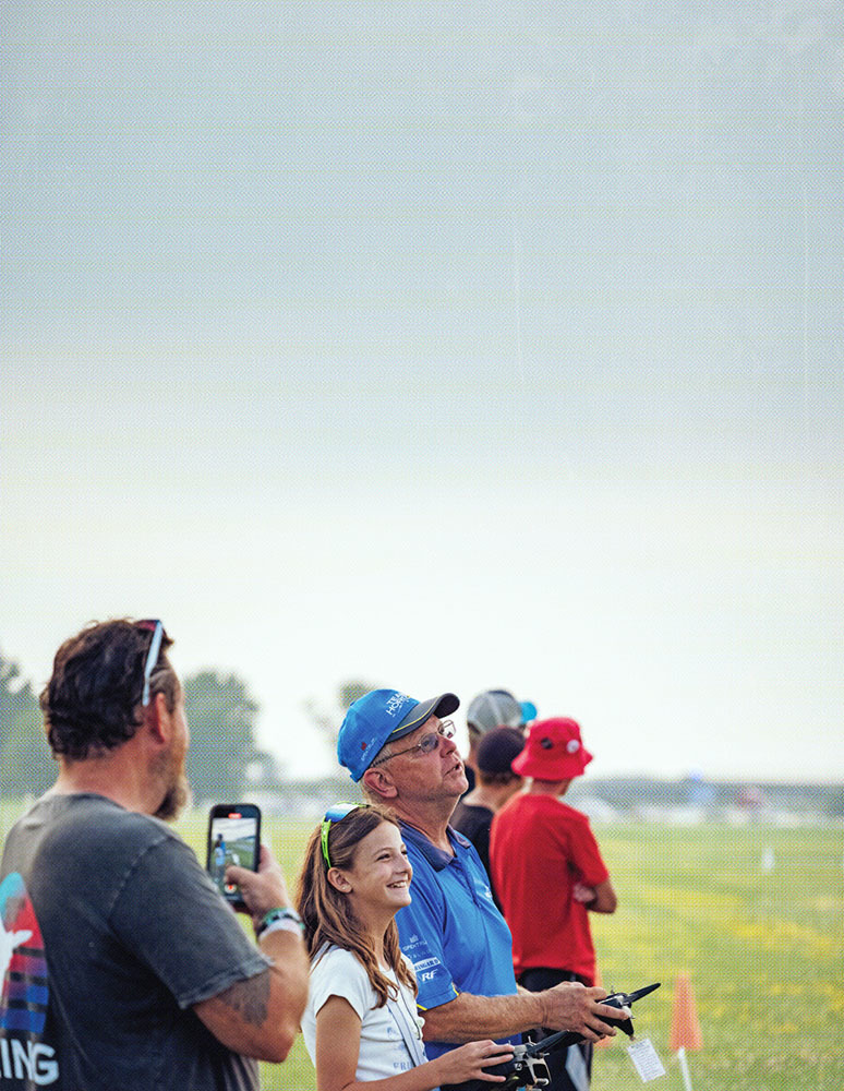 People watching the sky at a field; one holds a phone, another a remote control.