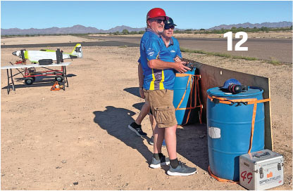 Two men in blue shirts fly a model plane in a desert area.