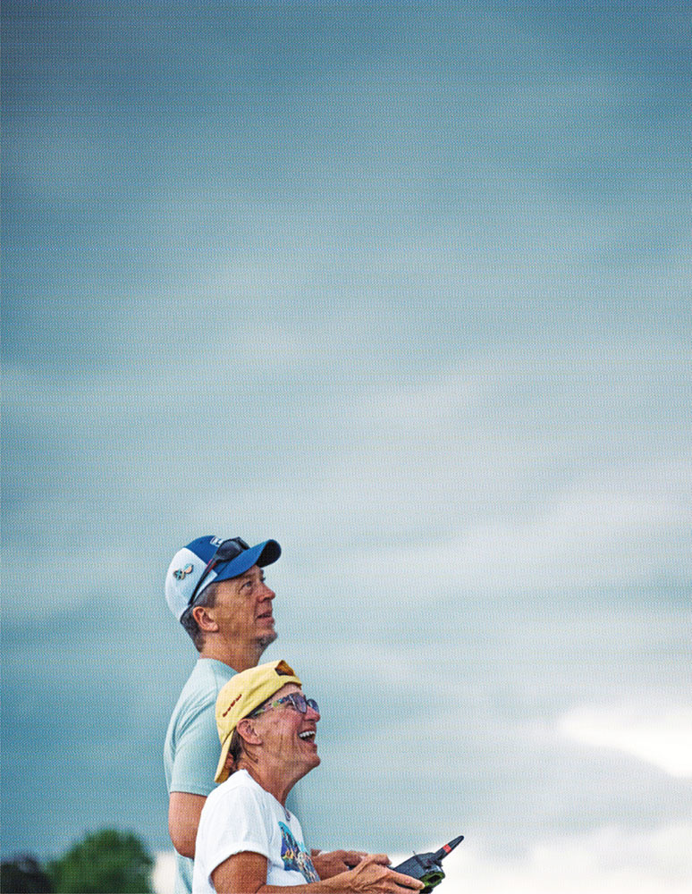 Two people with remote controls, smiling, looking up at a cloudy sky.