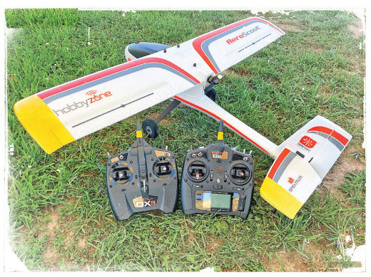 Toy plane with controllers on grass, labeled HobbyZone and AeroScout.