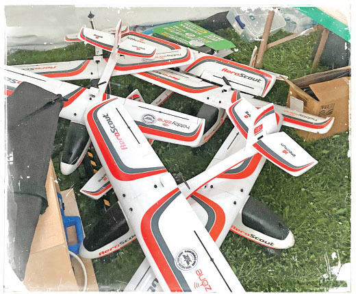 Stack of white and red AeroScout model planes on grass.
