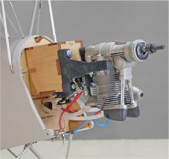 Small metal engine attached to a wooden frame with wires, against a gray background.