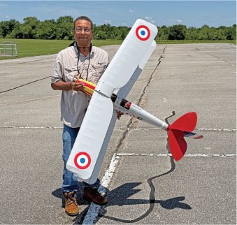 Man holding a large model airplane on a sunny day, standing on a tarmac.