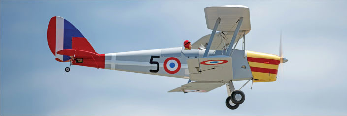 Vintage biplane with French colors and number 5 flies in blue sky.