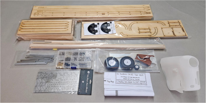 Model airplane kit parts, including wooden sheets, screws, gears, wheels, and instruction sheet.