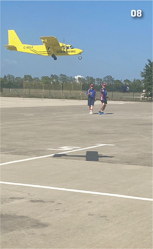Yellow plane flying over two people on a concrete runway; number 08 in corner.