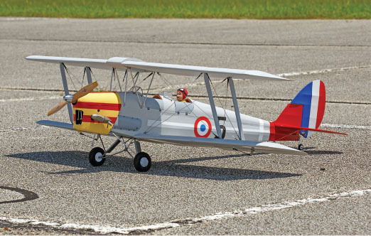 Model biplane on pavement, red and blue tail, with propeller and markings.