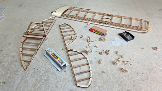 Wooden model airplane parts on a workbench with sandpaper and shavings.
