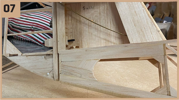 Wooden model structure with "Sulli" written inside, striped fabric in the background.