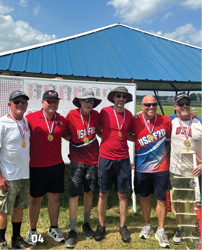 Men wearing medals, standing under a blue-roofed canopy, dressed in red USA shirts.