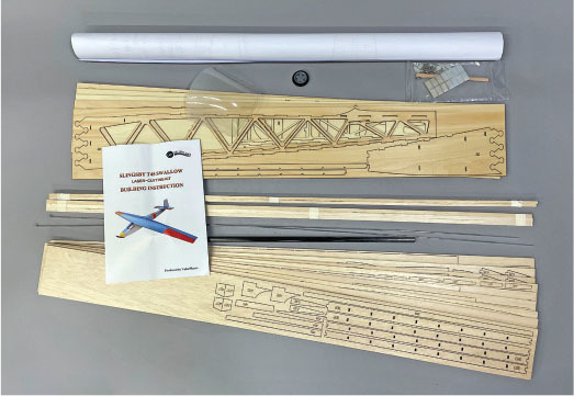 Model airplane kit with wooden parts, rolled plans, and an instruction booklet.