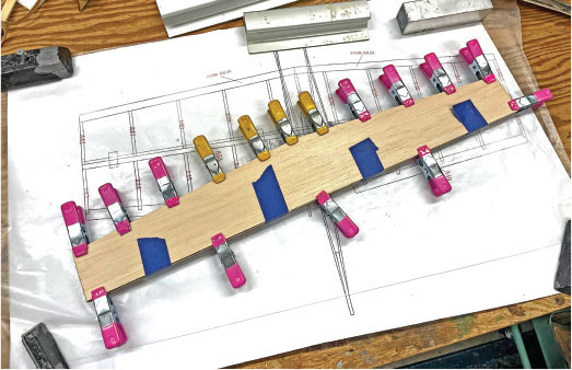 Wood piece clamped on blueprint with pink and yellow clips.