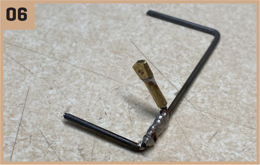 Bent metal rods and a small bolt on tile; number "06" in the corner.